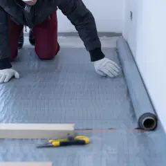 Pracownik układa folię pod styropian. To kluczowy etap izolacji podłogi.