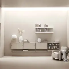 Minimalistiskt vardagsrum med stringhylla, beigefärgad förvaring, fåtölj och lampa.