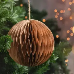 Brązowa, papierowa ozdoba choinkowa w kształcie kuli, wisząca na gałęziach choinki.