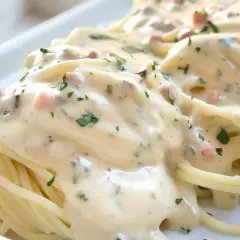 Spaghetti mit cremiger Carbonara-Sauce und Speckstücken, garniert mit Petersilie.