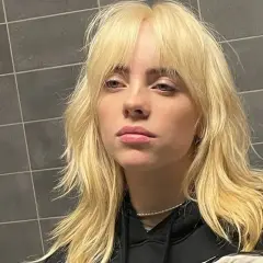 Blond włosy w stylu wolf cut, z grzywką i warstwami, opadające na ramiona.