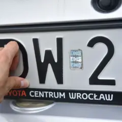 Dłoń poprawia hologram na tablicy rejestracyjnej DW 29. To ważny element potwierdzający legalność pojazdu.