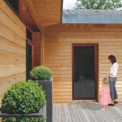 Piękna drewniana elewacja i taras, świadczące o starannej impregnacji drewna. Kobieta z dzieckiem na tle nowoczesnego domu.