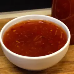 En skål med söt chili sås, med en flaska i bakgrunden. Perfekt för dippning eller som smakförhöjare.