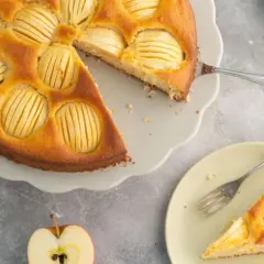 Omas weltbester Apfelkuchen, goldbraun gebacken, mit saftigen Apfelscheiben. Ein Stück auf einem Teller mit Gabel daneben.
