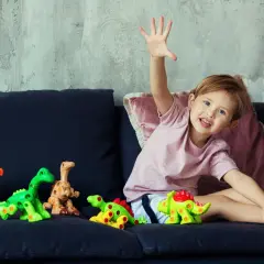Uśmiechnięte dziecko z zabawkami-dinozaurami na kanapie.