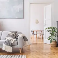 Un salón moderno con sofá gris, manta, cojín, mesa de café y piano negro. La luz blanca ilumina el espacio, creando una atmósfera acogedora.