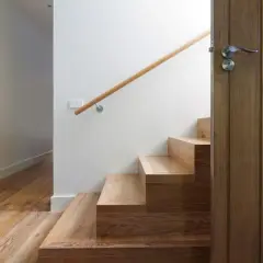 Escalier en bois clair, parfait pour un entretien facile. Une porte en bois sombre s'ouvre sur la cage d'escalier.
