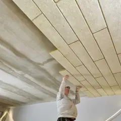 Pracownicy montują płyty izolacyjne, wykonując ocieplenie stropu betonowego.