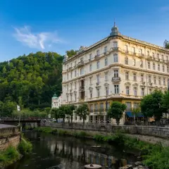 Eleganckie budynki w Karlowych Warach nad rzeką, otoczone zielenią. Urokliwe karlowe wary termy zachęcają do relaksu.
