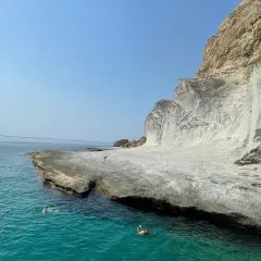 Dos personas nadan en las **calas agua amarga**, con acantilados blancos y mar turquesa bajo un cielo azul.