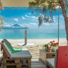 Relaks przy plaży w Armenistis Camping. Leżaki, stolik z owocami i widok na morze z górą w oddali.