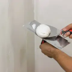 Mani che usano una spatola per applicare lo stucco bianco su un muro.