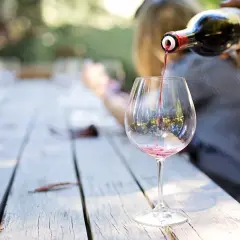 Un verre se remplit de vin rouge, versé d'une bouteille sur une table en bois. Un moment de partage, un vin tourné.
