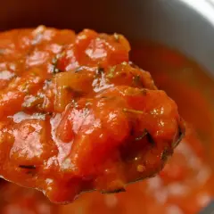 Cuchara llena de passata de tomate casera, con trozos de tomate y hierbas aromáticas.