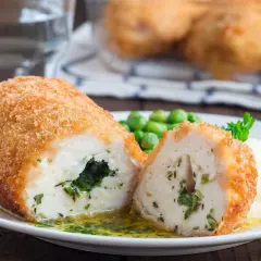Pyszny kotlet po kijowsku, chrupiący z zewnątrz, soczysty w środku, z zielonym nadzieniem. Podany z puree i groszkiem.