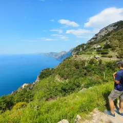 Hiker on a cliff path overlooking the blue sea and coastline.