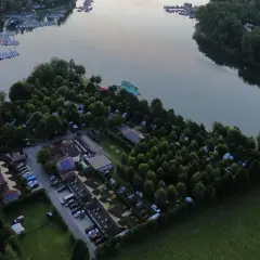 Malowniczy widok na camping w Polańczyku nad jeziorem, z łodziami na wodzie i zielonymi drzewami.