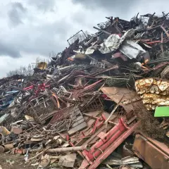 Góra złomu, gdzie można sprawdzić skup akumulatorów cena za kg. Widoczne różne rodzaje metali, siatki, części maszyn.