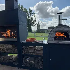 Un grand barbecue et un four à pizza en pierre s'apprêtent à faire un barbecue sous un ciel bleu et nuageux.