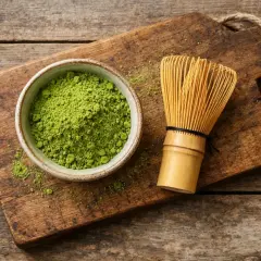 Schüssel mit feinem Matcha-Pulver und Bambusbesen auf Holzbrett. Ideal für ein gesundes Getränk mit wenigen matcha kalorien.