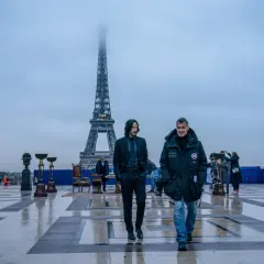 Dwóch mężczyzn idzie po placu przed wieżą Eiffla w Paryżu.