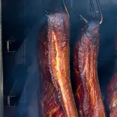W jakiej temperaturze wędzić boczek? Kilka kawałków wędzonego boczku w wędzarni, otoczonych dymem.