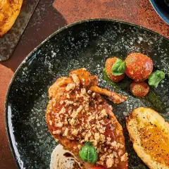Wykwintny kurczak supreme w sosie, z chrupiącą posypką, podany z pieczonym ziemniakiem i pomidorkami koktajlowymi.