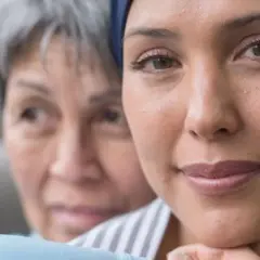 Deux femmes se serrent l'une contre l'autre. L'une porte un foulard, peut-être en raison de sa chimio, et a quelques boutons sur le visage.