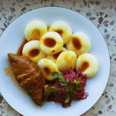 Kluski śląskie z roladą i czerwoną kapustą na talerzu.