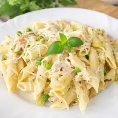 Penne z kremowym sosem, kawałkami szynki, groszkiem i startym parmezanem, udekorowane listkiem bazylii. Pyszny makaron z szynką.