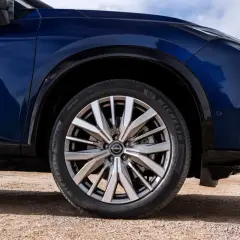 Błękitny Nissan X-Trail na drodze gruntowej, z widocznym kołem i fragmentem nadwozia.