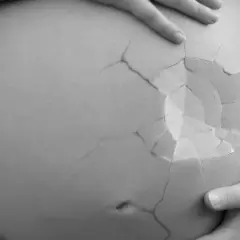En gravid mage med sprickor som ett äggskal, en symbol för ett tidigt missfall och den sorg det medför.