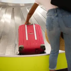 Kobieta odbiera czerwoną walizkę z taśmy bagażowej. Mam nadzieję, że nie będzie opóźniony bagaż odszkodowanie.