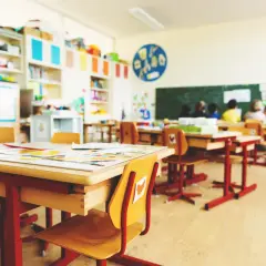 Einladende Raumgestaltung im Klassenzimmer: Helle Tische, bunte Bücherregale und Kinder, die lernen.