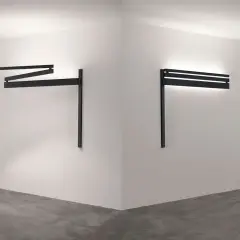 Dos apliques de pared regulables negros, uno extendido en zigzag y otro horizontal con luz indirecta, iluminan un rincón minimalista.