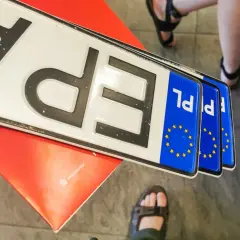 Kilka nowych tablic rejestracyjnych PL leży na czerwonym podkładzie.