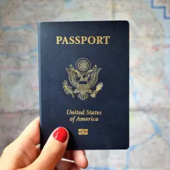 Dłoń trzyma paszport USA na tle mapy. Zastanawiasz się, ile trwa wyrobienie paszportu w trybie przyspieszonym?