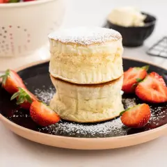 Två fluffiga japanska pannkakor staplade på en tallrik med färska jordgubbar och pudersocker.