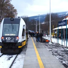Pociąg KD z napisem "Świeradów Zdrój" na stacji. W tle góry i budynek dworca.