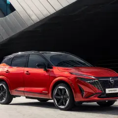 Czerwony Nissan Qashqai prezentuje swoje nowoczesne linie i imponujące nissan qashqai wymiary. Stylowy SUV na tle architektonicznej fasady.