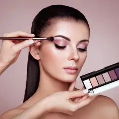 Kobieta zmysłowo maluje powieki, tworząc efekt latte makeup. W dłoni trzyma paletę cieni do powiek.