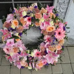 Wieniec pogrzebowy dla młodej osoby, pełen różowych lilii, róż i gerber, spoczywa na kamiennej płycie nagrobnej.