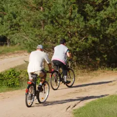 Dwie osoby na rowerach odkrywają najładniejsze trasy rowerowe na Mazowszu, jadąc piaszczystą drogą wśród drzew.