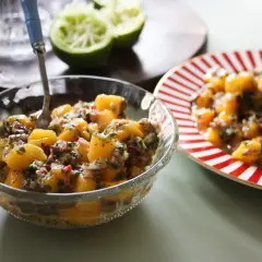 En skål med färgglad mangosalsa, med lime och en röd-vit randig tallrik i bakgrunden.
