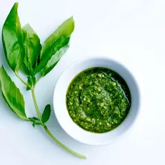 Färskt basilika bredvid en skål med hemlagad pesto. Ett perfekt pesto recept för sommaren.