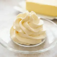 Puszysta masa budyniowa z mascarpone, udekorowana na talerzyku. W tle kostka masła.
