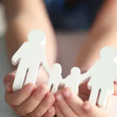 Hände halten weiße Holzfiguren einer Familie. Dies symbolisiert die Verantwortung für ein Kind und die finanzielle Unterstützung, die damit einhergeht.