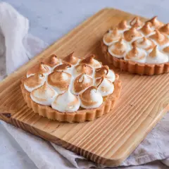 Due crostatine con crema al limone e meringa all'italiana, dorata e soffice, su un tagliere di legno.