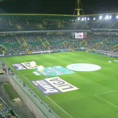 Widok na pełny stadion Sporting Lizbona, z zieloną murawą, trybunami wypełnionymi kibicami i reklamami na boisku.